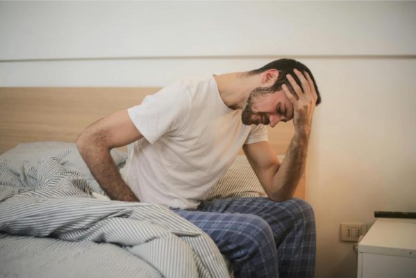 loan fatigue image of man holding his head sitting on bed